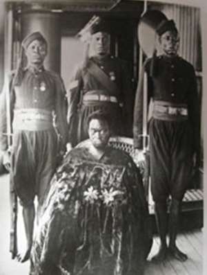 Oba Ovonramwen, during whose reign the British looted the Benin Bronzes, with guards on board a ship on his way to exile in Calabar in 1897. The gown he is wearing hides his shackles. Photograph by the Ibani Ijo photographer J. A. Green. From the Howie photo album in the archives of the Merseyside Maritime Museum.