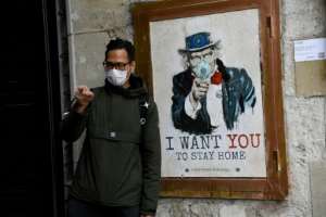 A man wearing a face mask poses with a poster by artist TVBoy in Barcelona, where authorities have ordered a widespread shop closure.  By Josep LAGO (AFP)