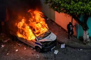 A masked man holding a shotgun walks past a burning police vehicle during clashes between Algerian protesters and riot police in Algiers. By RYAD KRAMDI (AFP)