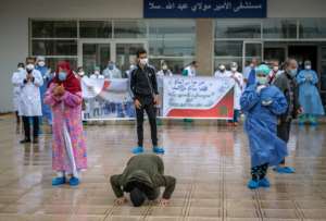 A patient who recovered from Covid-19 kisses the ground and another rejoices with medical staff as they leave a hospital in the city of Sale, north of the Moroccan capital Rabat.  By FADEL SENNA (AFP)