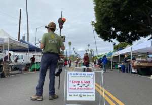 A staff member of the Mar Vista Farmers Market makes sure people stay six feet apart from each other using a bullhorn and a 6-foot pole in Mar Vista, California.  By Chris DELMAS (AFP)