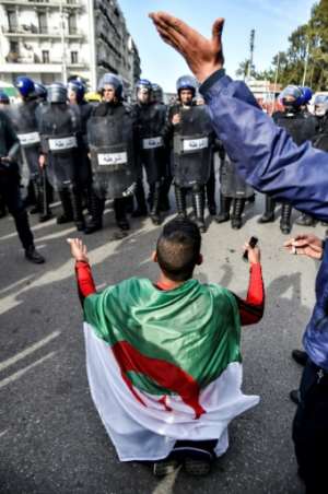 An Algerian youth draped in a national flag chants slogans while kneeling before riot police. By RYAD KRAMDI (AFP)