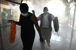 In Nairobi, public transport is operational, but passengers walk through a disinfectant tunnel as they prepare to board a commuter train at the main railway station before curfew.  By SIMON MAINA (AFP)