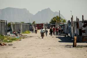Residents of Blikkiesdorp walk past houses and corrugated iron shacks.  By GIANLUIGI GUERCIA (AFP)
