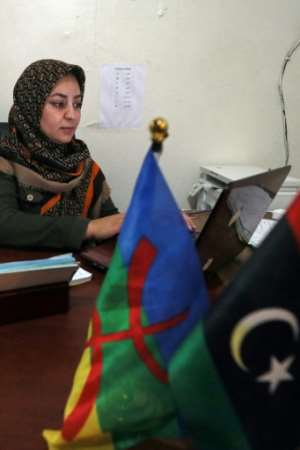 School director Sondoss Saki sits at a desk with both Libyan and Amazigh (Berber) flags.  By Mahmud Turkia (AFP)