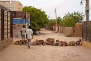 Sudanese walk past a brick roadblock in Omdurman, Khartoums twin city.  By - (AFP)
