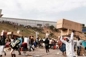 Suspected looters carry goods from the Game Warehouse in Durban.  By - (AFP)
