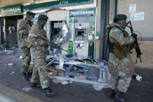 Troops walk past the remains of an automated teller machine (ATM) in the Diepkloof Square mall in Soweto.  By Phill Magakoe (AFP)