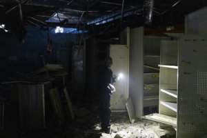 Aftermath: A woman uses a torch to clear debris at a looted shop in Durban's Dube Village Mall. By GUILLEM SARTORIO AFP