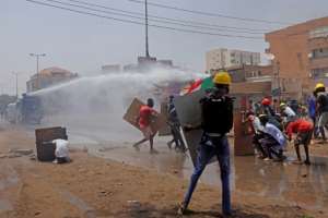 Sudanese anti-coup protesters take cover as riot police try to disperse them with a water cannon during a demonstration against military rule in Khartoum on June 30. By - AFP