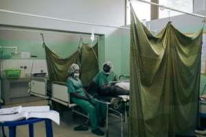Two nurses sit beside a patient recovering from surgery. By ALEXIS HUGUET AFP