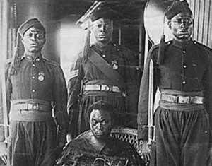 Oba Ovonramwen, during whose reign the British looted the Benin Bronzes with guards on board ship on his way to exile in Calabar in 1897. The gown he is wearing hides his shackles. Photograph by the Ibani Ijo photographer J. A. Green. From the Howie photo album in the archives of the Merseyside Maritime Museum