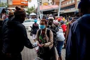 A taxi rank marshal sprays hand sanitiser on a commuter wearing a mask as a preventive measure as she arrives at the Wanderers taxi rank in Johannesburg. - Source: Marco LongariAFP via Getty Images