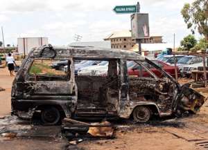 A woman walks near a minibus burnt by an angry mob in reaction to suicide bomb attacks.  By Victor Ulasi (AFP)