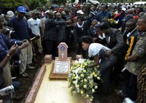 The widow of Kenyan marathon champion Samuel Kamau Wanjiru, Tereza Njeri (to right of grave) lays a wreath.  By Tony Karumba (AFP)