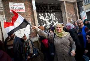 An Egyptian woman waves a national flag as she queues outside a polling centre to vote on a new constitution on January 14, 2014 in Mounira, a district of Cairo.  By Vriginie Nguyen Hoang AFP