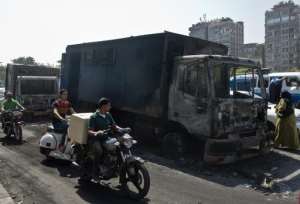 Egyptians ride past by a burnt-out police vehicle which was set on fire by Muslim Brotherhood supporters during clashes in Cairo, on October 7, 2013.  By Khaled Desouki AFP