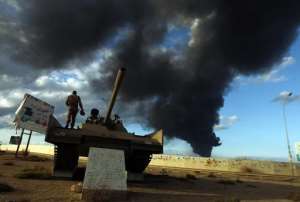A member of the Libyan army stands on a tank as heavy black smoke rises after a fire broke out at a car tyre disposal plant during clashes against Islamist gunmen in Benghazi on December 23, 2014.  By Abdullah Doma AFP