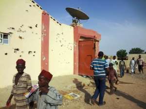 Residents of Kano, Nigeria, walk past the bullet-riddled wall of a hideout of Al-Qaeda-linked abductors in May 2012.  By Aminu Abubakar (AFP/File)