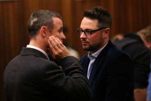 Olympic and Paralympic track star Oscar Pistorius (L) speaks to his brother Carl during his murder trial at the North Gauteng High Court in Pretoria on May 20, 2014. By Siphiwe Sibeko (POOL/AFP/File)