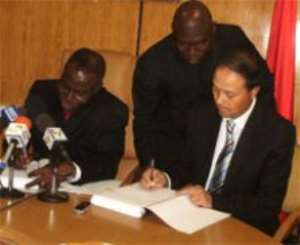 Dr Joe Oteng-Adjei left, appending his signature to the agreement while Mr Yu Guohui right initials for his Group. Looking on is a Deputy Energy Minister, Alhaji Inusah Fuseini.