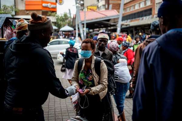 A taxi rank marshal sprays hand sanitiser on a commuter wearing a mask as a preventive measure as she arrives at the Wanderers taxi rank in Johannesburg. - Source: Marco Longari/AFP via Getty Images