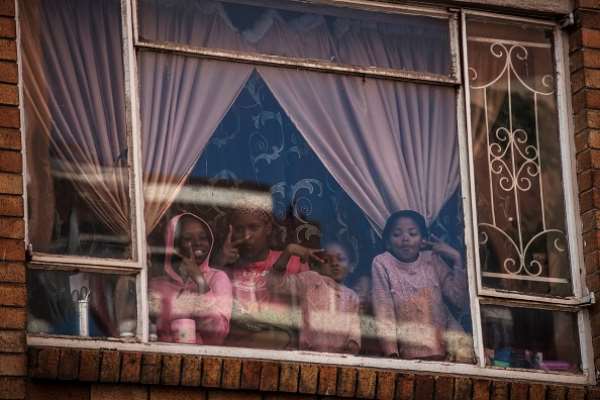 Children at window of a building in Hillbrow, Johannesburg. Children will be vulnerable if vaccinations are postponed. - Source: Photo by Marco Longari/AFP via Getty Images