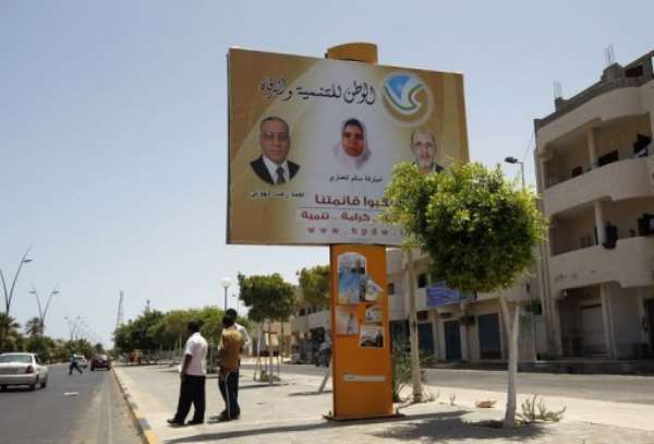 Libyan men stand near an election campaign poster in Sirte. By Mohammed Abed (AFP)