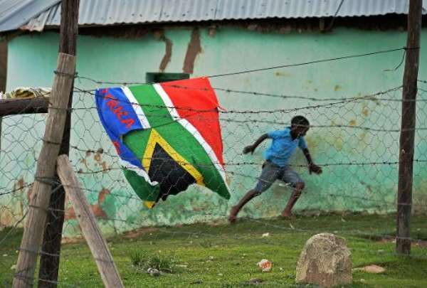 A boy runs past a South African flag near the former home of the late former South African president Nelson Mandela in Qunu on December 9, 2013. By Carl de Souza (AFP)