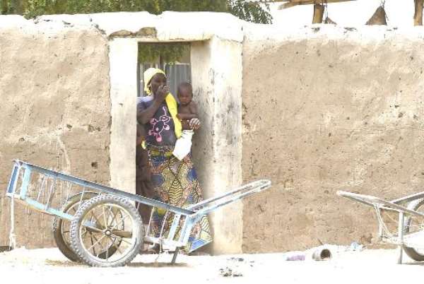 A woman and her baby stand in the doorway of their home in Malam Fatori. By (AFP)