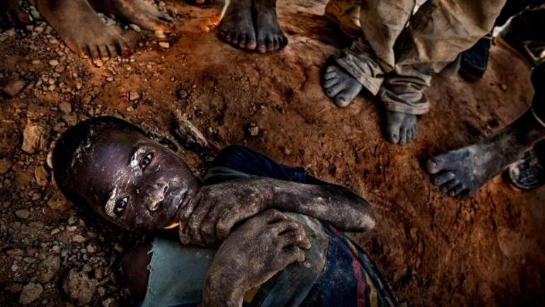 A young boy lies exhausted on the ground in a gold mine in Burkina Faso