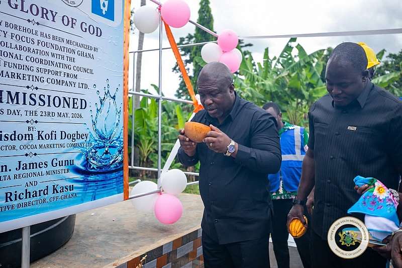 The Volta Regional Minister, drinking water from the newly commissioned mechanised borehole at Dodome-Dogblome accompanied by the Managing Director of the Ghana Cocoa Marketing Company.