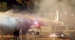 Protesters stand behind a makeshift shield as they face off with police water canon during an anti-government demonstration in central Tirana on October 16, 2026. -  Adnan Beci, AFP