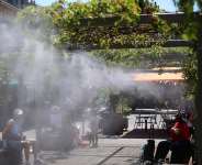 People sit in a shaded area under a water mist system to cool off in Bordeaux, south-western France, 17 June. - AFP - ROMAIN PERROCHEAU