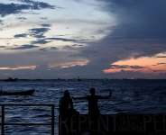People sit on the seawall as the sun sets in Georgetown, Guyana,  Nov. 19, 2024. -  Matias Delacroix, AP