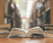 Book in library with old open textbook, stack piles of literature text archive on reading desk, and aisle of bookshelves in school study class room background for academic education learning concept - Shutterstock