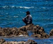 A migrant who crossed into Spain from Morocco sits on a shore in the Spanish enclave of Ceuta, Sunday, Aug. 2, 2026. -  Antonio Sempere, AP