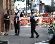 Police community support officers (PCSOs) stand behind cordon tape at Endell road in Covent Garden, central London on August 5, 2026. -  Henry Nicholls, AFP