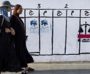 Women in Rabat walk past a wall displaying electoral symbols used by political parties participating in Moroccos legislative elections. - AFP - ABDEL MAJID BZIOUAT