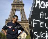 A firefighter stands next to a coffin-shaped sign reading Death by fire, suicide in front of the Eiffel Tower during a demonstration entitled the Reinforcement Column of Anger at the Champs de Mars in Paris, on 27 September, 2026. -  AFP - Julien de Rosa