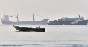 A small boat moves along the shoreline where an a cargo vessel, tugboat and industrial barge are all anchored in the Strait of Hormuz off Bandar Abbas, Iran,June 1, 2026 -  AP