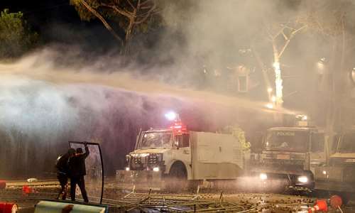 Protesters stand behind a makeshift shield as they face off with police water canon during an anti-government demonstration in central Tirana on October 16, 2026. -  Adnan Beci, AFP