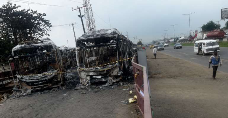 People in Lagos on October 26, 2020, walk past buses burnt during a protest against police brutality. Nigerian President Muhammadu Buhari on October 25 appealed for