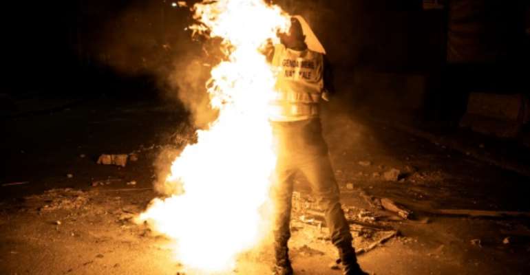 A police officer caught fire while trying to extinguish a burning tyre. By JOHN WESSELS (AFP)