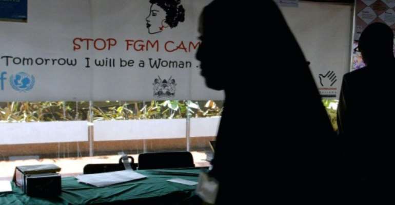 A young woman walks past a banner against female genital mutilation. By SIMON MAINA (AFP/File)
