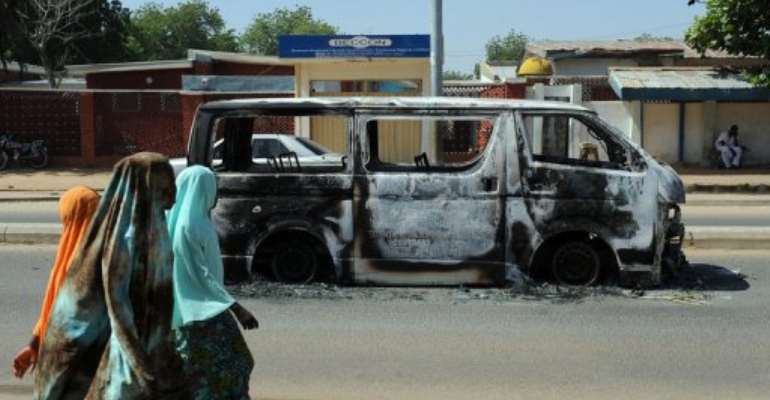 Young girls walk past a vehicle burnt in 2011 on a street in Damaturu in northeastern Nigeria. By Pius Utomi Ekpei (AFP/File)