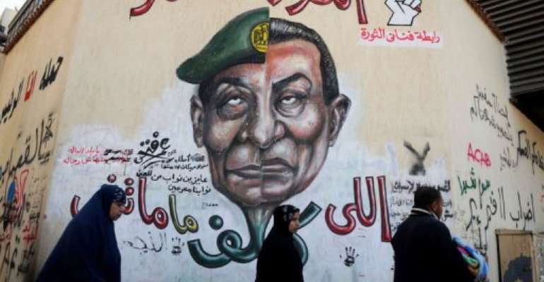 Egyptians walk past graffiti with a slogan reading,