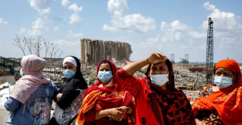 Lebanese women (L) and South Asian foreign workers (R) look on as they stand before the ravaged port of Lebanon's capital Beirut on August 9. By PATRICK BAZ (AFP)