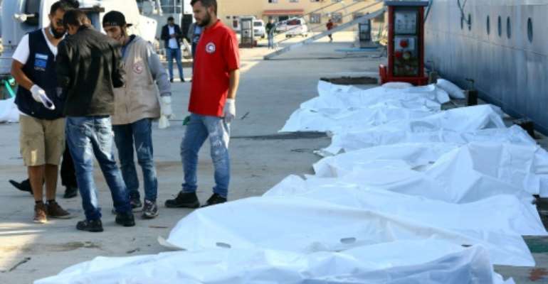 Libyan paramedics and aid workers stand next to the bodies of African migrants at a naval base in Tripoli on November 25, 2017, after more than 30 migrants died off the coast of Garabulli, 60 kilometres (40 miles) east of the capital. By MAHMUD TURKIA (AFP)