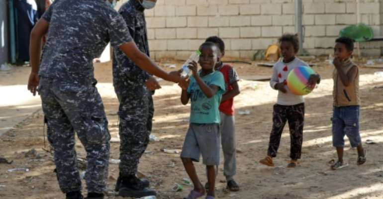 Libyan security forces hand water to children as African migrants gather at a makeshift shelter near Tripoli on October 11, 2021. By Mahmud Turkia (AFP/File)